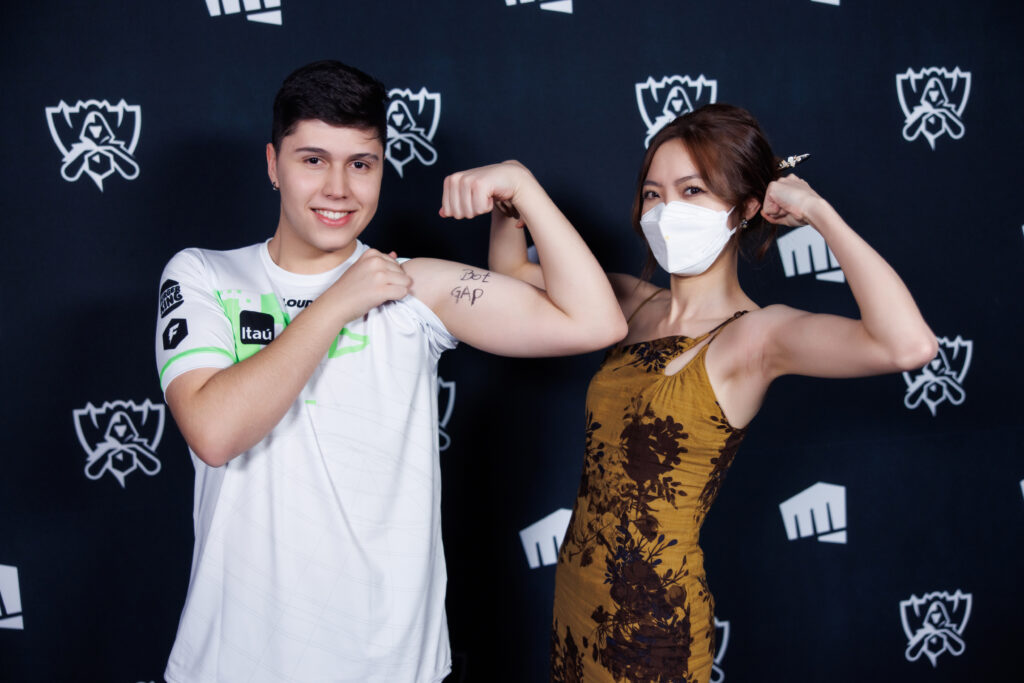 Image shows LOUD player Brance and female Asian translator at Worlds 2022. Both are flexing their arms. "Bot Gap" is written on Brance's bicep.